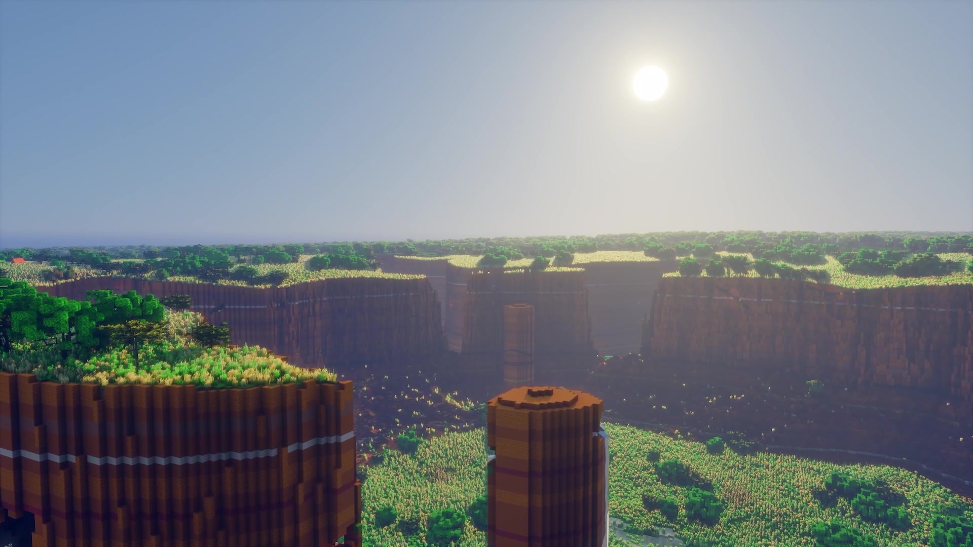 The sun low over a wide canyon, rock pillars in the foreground